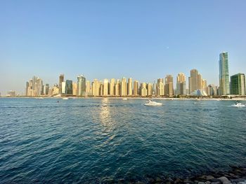 Sea by modern buildings against clear sky