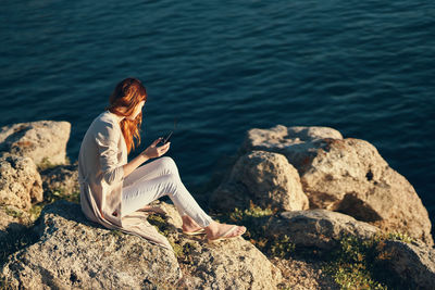 Woman sitting on rock by sea