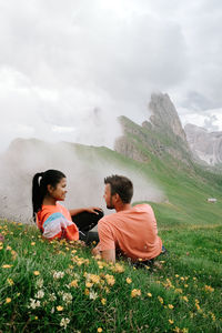 Rear view of friends sitting on land against sky