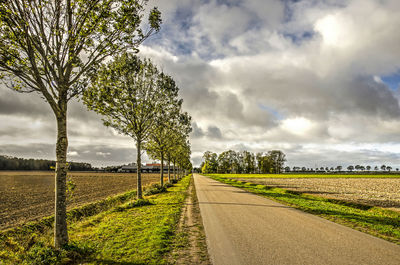 Empty road amidst field against sky