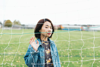 Portrait of woman seen through net while standing on sports field