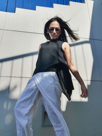 Young woman wearing sunglasses standing against wall