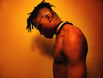 Portrait of shirtless man looking away against orange wall