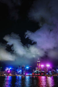 Illuminated buildings by river against sky at night