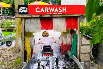 Rear view of boy riding bicycle by car wash sign board