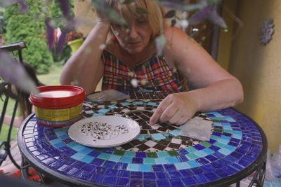 Mature woman with small tiles placing on mosaic table