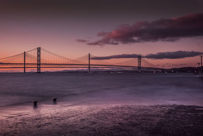 Suspension bridge over river against cloudy sky