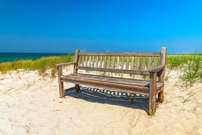 Empty benches on beach against blue sky