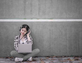 Full length of smiling girl sitting on wall