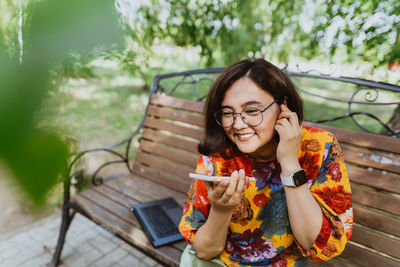 Cheerful adult lady with glasses engaged in phone conversation while seated in park