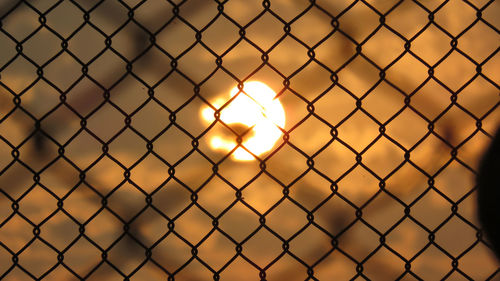 Close-up of chainlink fence against sunset sky