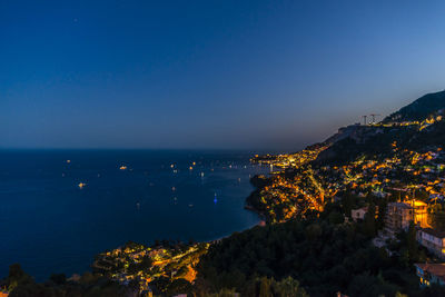 Illuminated city by sea against blue sky