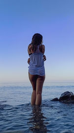 Rear view of woman standing in sea against clear sky