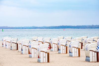 Hooded chairs on beach against sky
