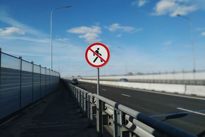 Road sign on bridge against sky