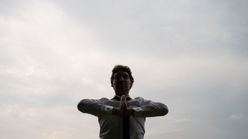 Low angle view of man with hands clasped standing against sky
