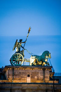 Low angle view of illuminated statue on brandenburg gate against sky at dusk