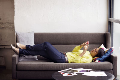 Side view of woman using smart phone while lying on sofa in office