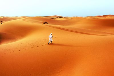 Rear view of man walking in desert against clear sky