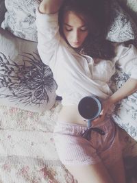 Beautiful young woman holding coffee cup while resting in bed