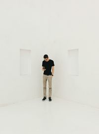 Man using phone while standing in corner of white room