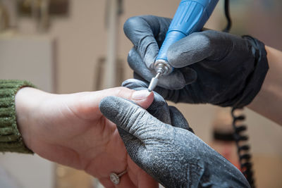 The manicurist grinds off the old coating with professional electric nail file.