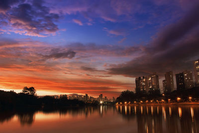 Scenic view of lake by buildings against sky during sunset