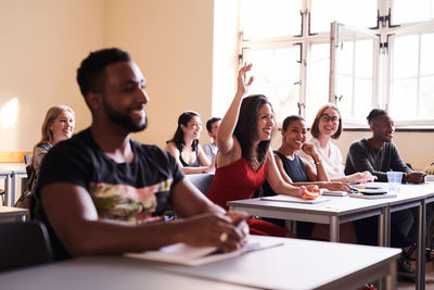 Happy woman raising arm to answer in language class