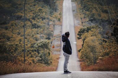 Rear view of man standing on road amidst trees