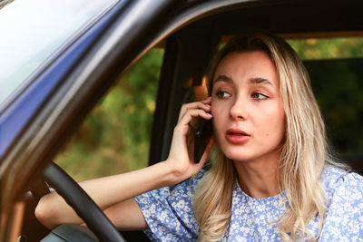 Young woman talking on a cell phone while sitting in the car in the driver's seat. attractive blonde