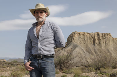 Adult man in cowboy hat in desert against rock and sky