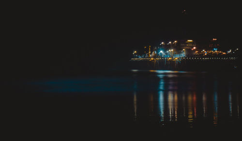 Illuminated city by sea against sky at night