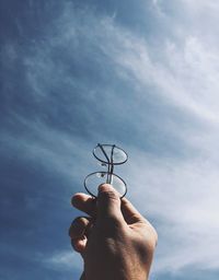 Low angle view of hand holding eyeglasses against sky