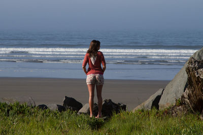 Rear view of woman standing on beach against sky