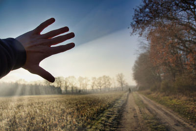 Cropped hand of man blocking sunbeam on field against sky