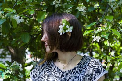 Young woman wearing flowers while standing against plants