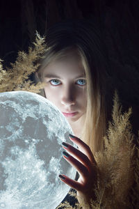 Digital composite image of young woman holding moon in darkroom