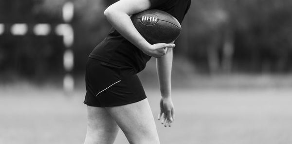 Midsection of woman holding american football while standing outdoors
