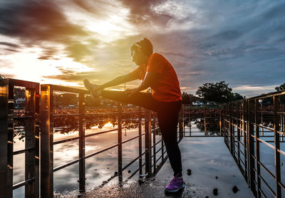 Man standing by railing against sky during sunset