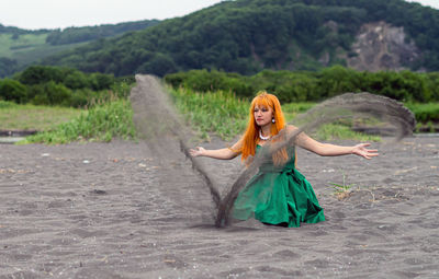 Woman playing with sand at beach against sky