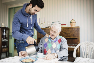 Caretaker serving coffee to senior man at nursing home