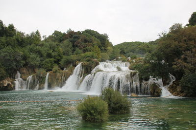 Scenic view of waterfall in forest against sky