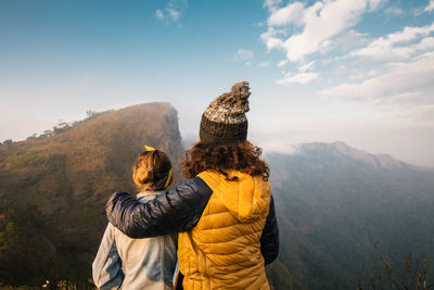 Rear view of mother and daughter standing on mountain against sky