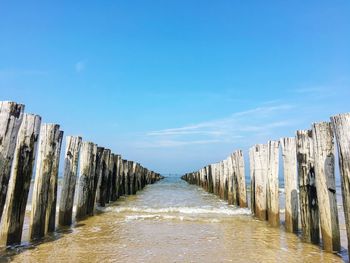 Wooden posts in sea against blue sky