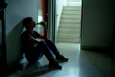 Man drinking beer while sitting on tiled floor