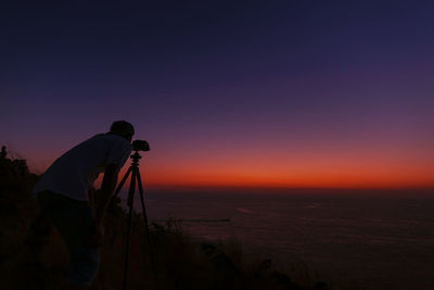 Side view of silhouette man photographing against dramatic sky at sunset