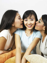 Happy friends kissing woman while siting on sofa at home
