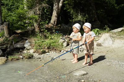 Two kids boys brothers twins fishing with a fishing rod on the mountain river on summer day