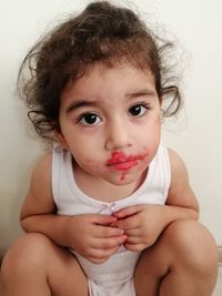 Portrait of cute baby girl with lipstick mess on face sitting against wall