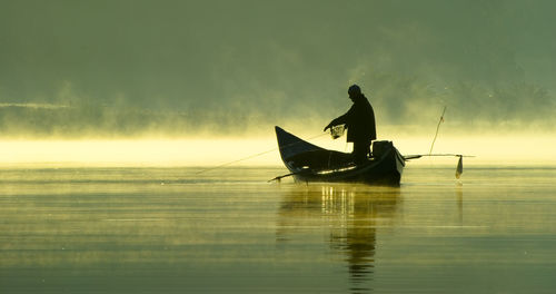 Silhouette people in boat on lake during sunset